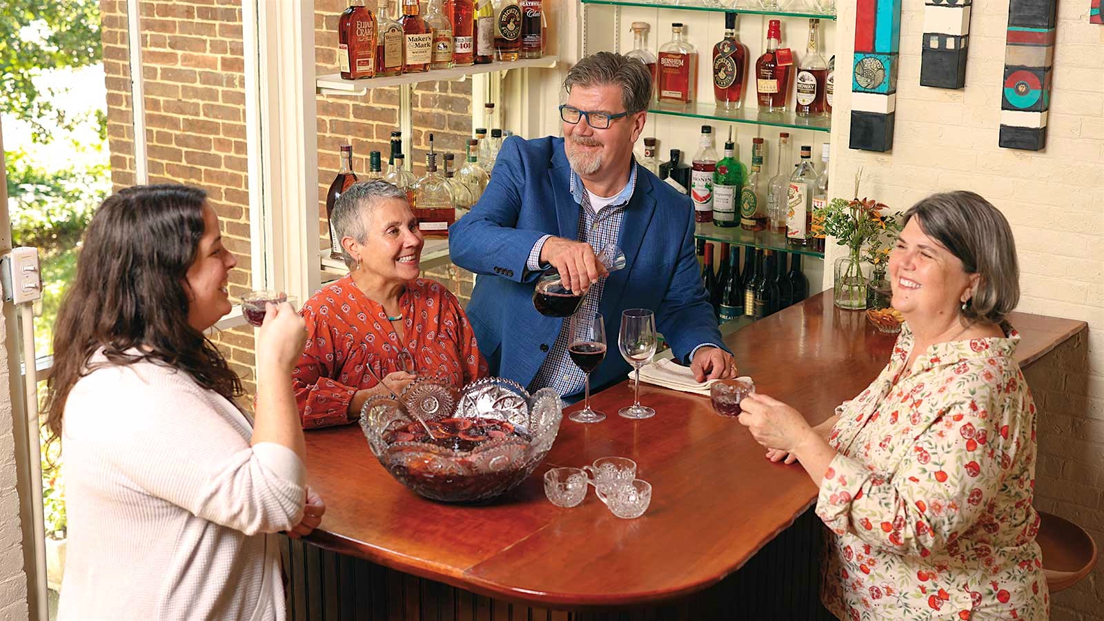 From left: Tali Schroeder, Donna Hecker, Chris Michel and Ouita Michel sit together at Holly Hill Inn drinking glasses of red wine from a decanter and punch from a bowl at the center of their table.